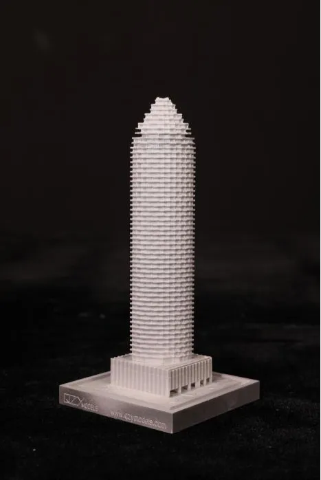 Maqueta blanca de precisión de un rascacielos cilíndrico alto con textura horizontal en capas, aguja puntiaguda cónica y base escalonada, montada sobre un pedestal transparente con la marca, sobre fondo negro: exhibición de un concepto de torre moderna minimalista de QZY Models.