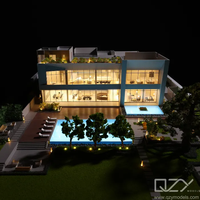 Maqueta de una villa moderna de lujo totalmente iluminada con interiores luminosos gracias a sus grandes paredes de cristal, terraza ajardinada en la azotea, piscina privada de borde infinito, jardín paisajístico con árboles, tumbonas y senderos iluminados: una exhibición arquitectónica residencial de alta gama de QZY Models.