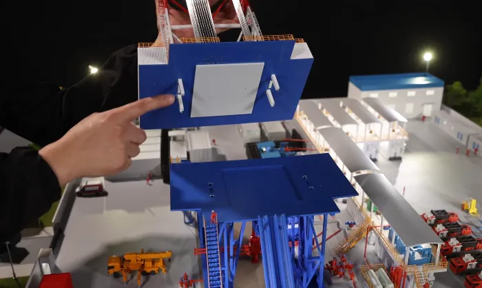 Quick connection design Hand demonstrating quick-connection modular blue platform section with white latches being attached to detailed drilling rig scale model – precise tool-free assembly of industrial platform module on illuminated oil & gas exhibition model